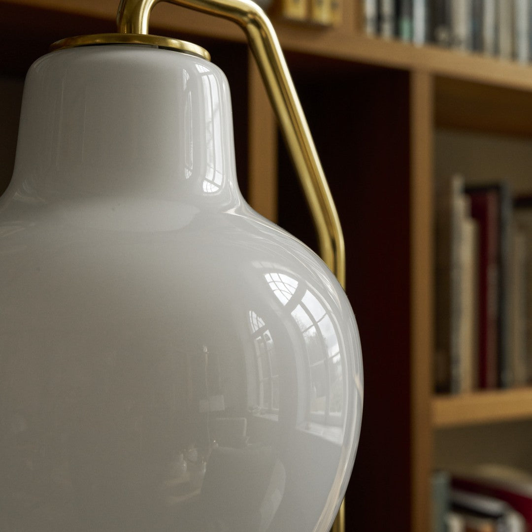 Close-up of a white lampshade with gold fixture against a blurred bookshelf background