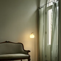 Vintage-style sofa in a room with a floor lamp and large window with curtains.