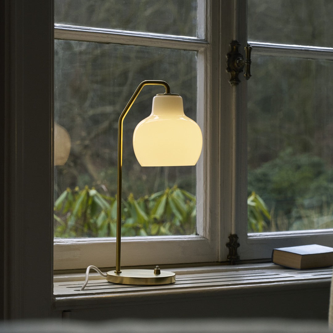 Table lamp with a warm glow on a windowsill with a blurred green outdoor background