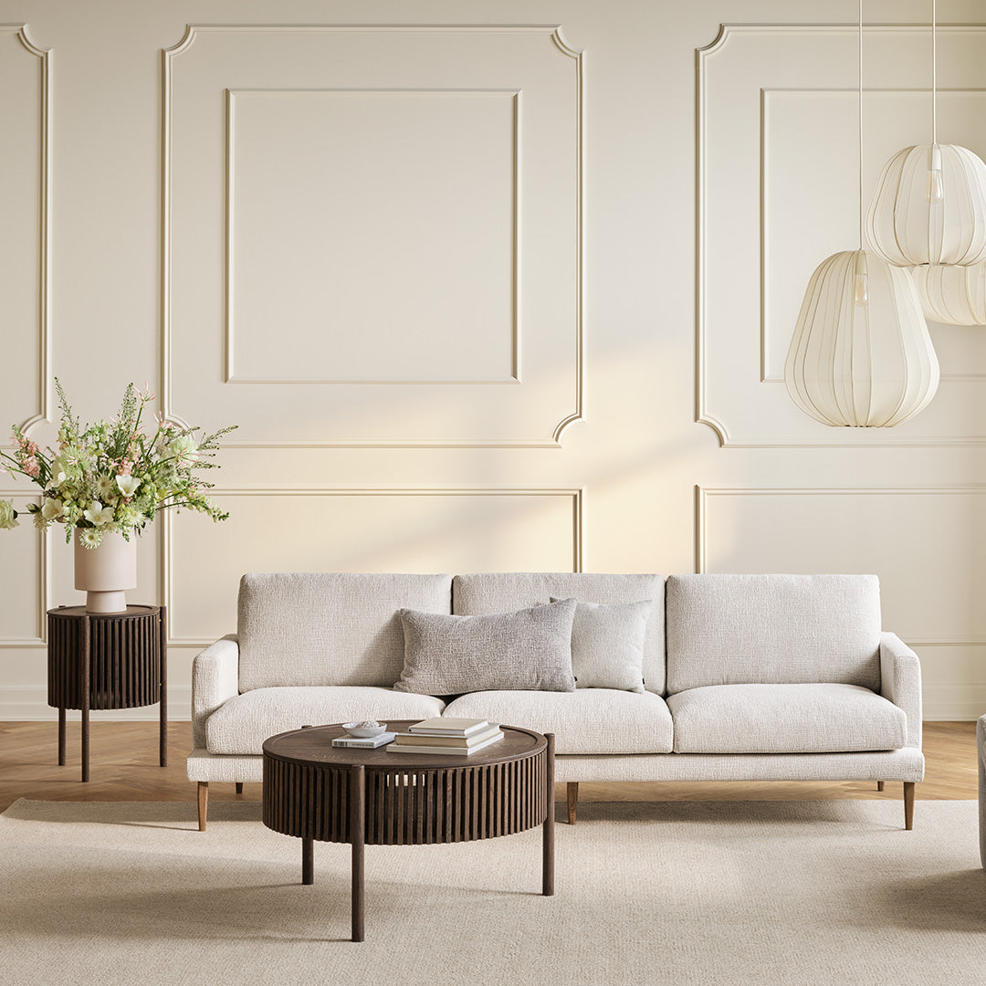 Beige modern sofa with gray accent pillow, paired with dark wood round table and light-colored decor in a neutral room.