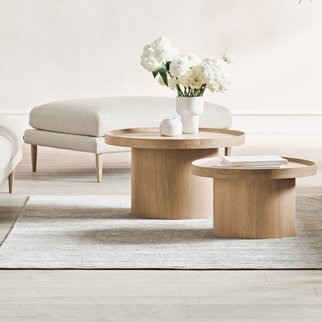 Natural wood coffee tables with smooth, round edges, complemented by a neutral-toned rug and soft beige upholstery.