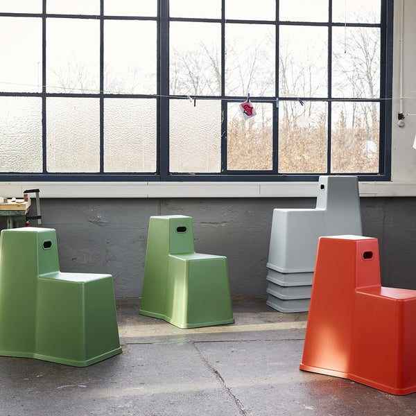 Colorful modern stacking stools in green, gray, and orange with a minimalist design against a bright window backdrop.