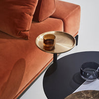 Rust orange velvet sofa with a sleek black and gold accent table, featuring contrasting round shapes and textures.