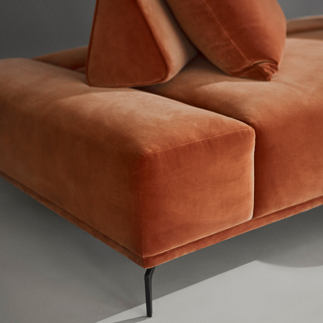 Rust-colored velvet sofa with smooth, soft surfaces and geometric shapes, ideal for modern interiors.