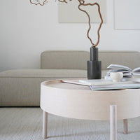 Light wood round coffee table with a smooth finish, complemented by a simple black vase and neutral-toned fabric sofa.