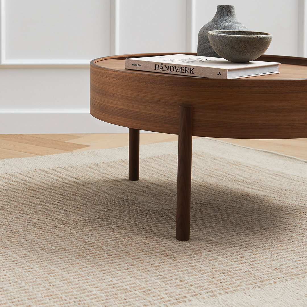 Round wooden coffee table with a deep brown finish atop a textured cream and beige patterned rug.