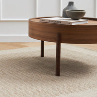 Round wooden coffee table with a deep brown finish atop a textured cream and beige patterned rug.