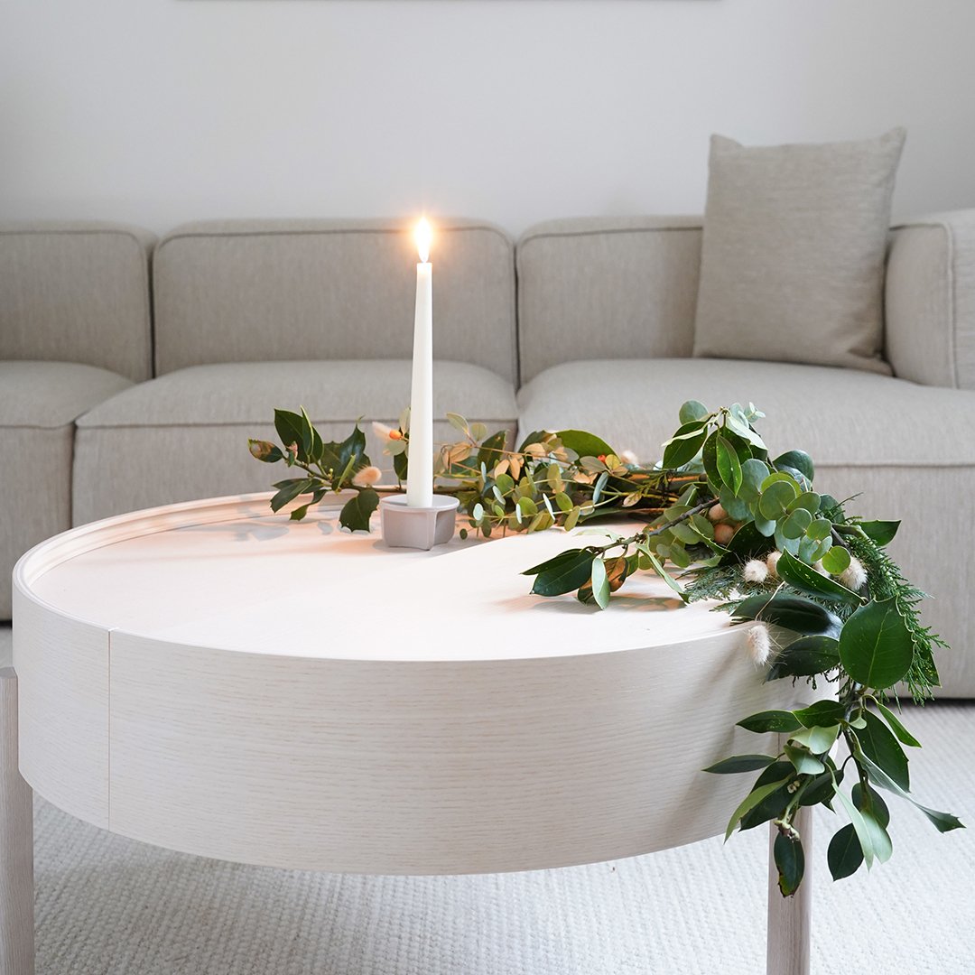 Modern beige round coffee table with a smooth surface, adorned with lush green foliage and a white candle.
