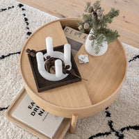 "Round wooden coffee table with natural oak finish, contrasting dark patterns, and white candle holders."
