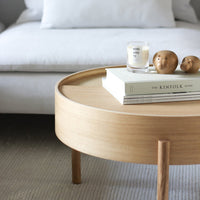 Light wood round coffee table with a smooth finish, featuring neutral-colored books and decorative objects on top.