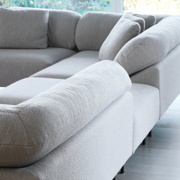 Light gray sectional sofa with textured fabric and soft curves, featuring minimalist design and neutral tones.