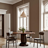 Minimalist dining room with a warm brown wall, black chairs, and a light beige pendant light above a wooden table.