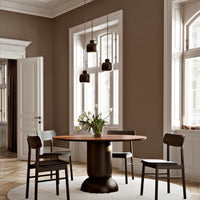 Elegant brown walls, round wooden table, black chairs, and stylish pendant lights create a modern, sophisticated dining space.
