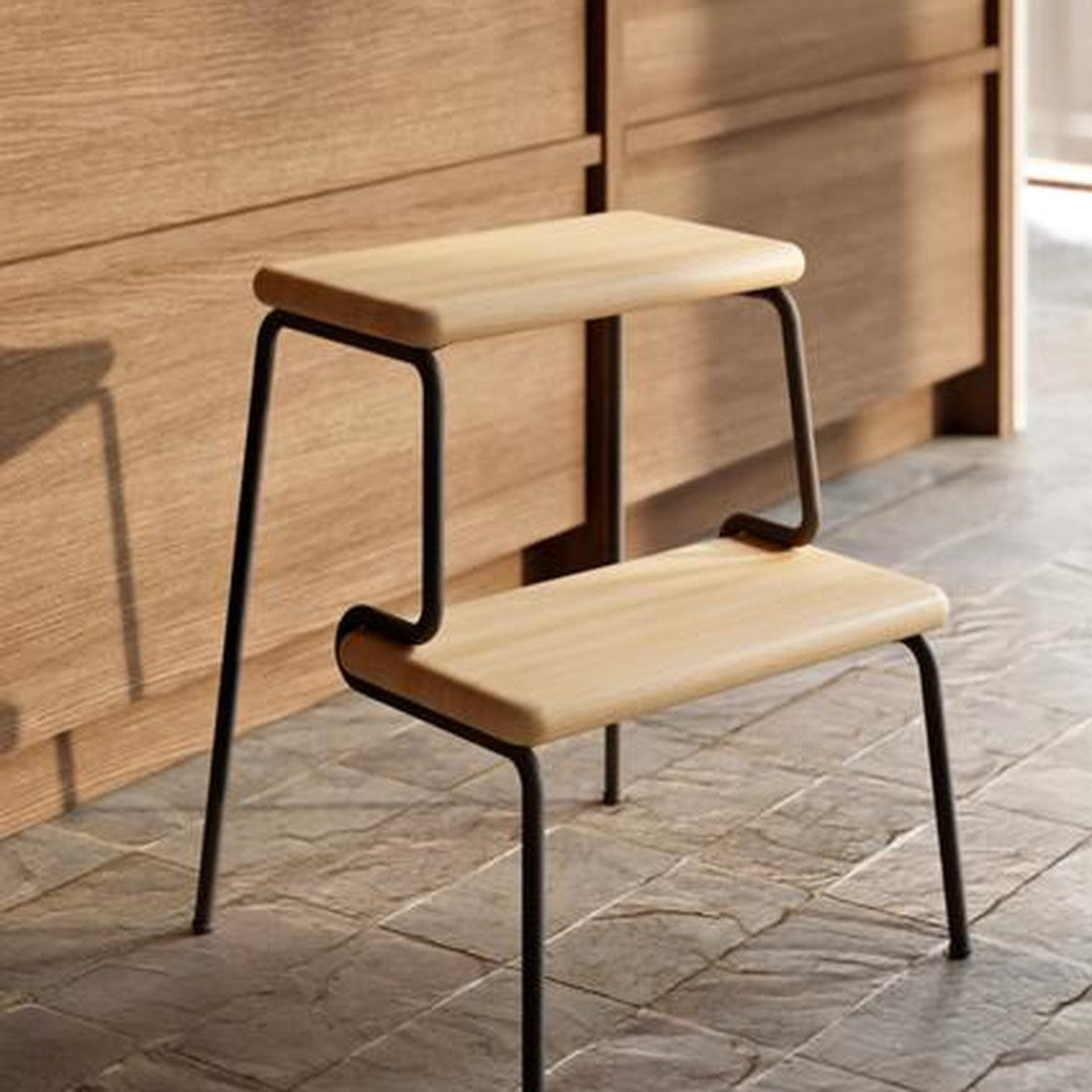 Wooden two-step stool with a light beige surface and black metal frame, set against a warm wood background.
