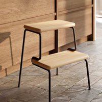 Wooden two-step stool with a light beige surface and black metal frame, set against a warm wood background.
