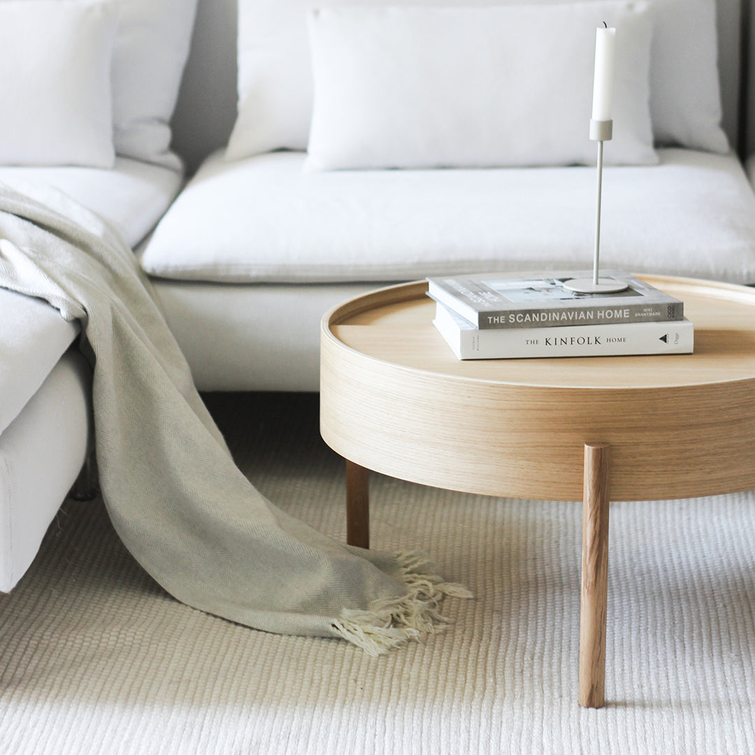 Light wood round coffee table with neutral beige throw and white sofa, featuring minimalist patterns and soft textures.