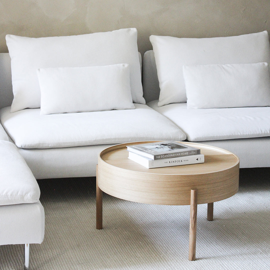 Round wooden coffee table with a natural finish, paired with white modern sofas and textured neutral background.