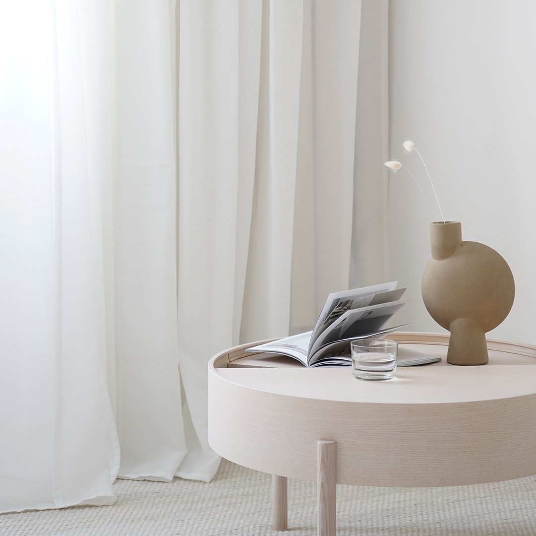 Neutral-toned round coffee table with a beige vase and soft white curtains, creating a serene, minimalist aesthetic.