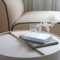 Neutral beige and white decor featuring a minimalist glass and textured books on a natural wood table.