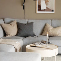 Light gray sectional sofa with beige and dark gray pillows, featuring a minimalist round coffee table. Soft, neutral colors.