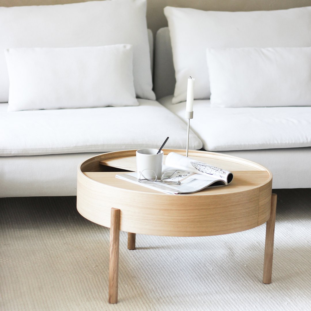 Light wooden round coffee table with a smooth finish, complemented by a neutral white sofa and textured rug.