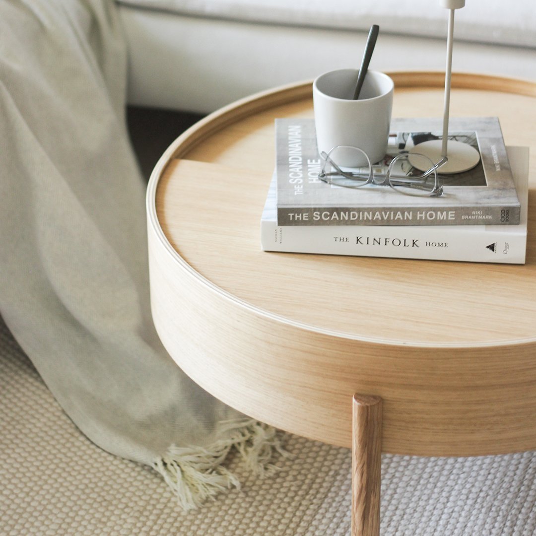Light wood round side table with natural finish, featuring soft gray decor and patterned textile accents.