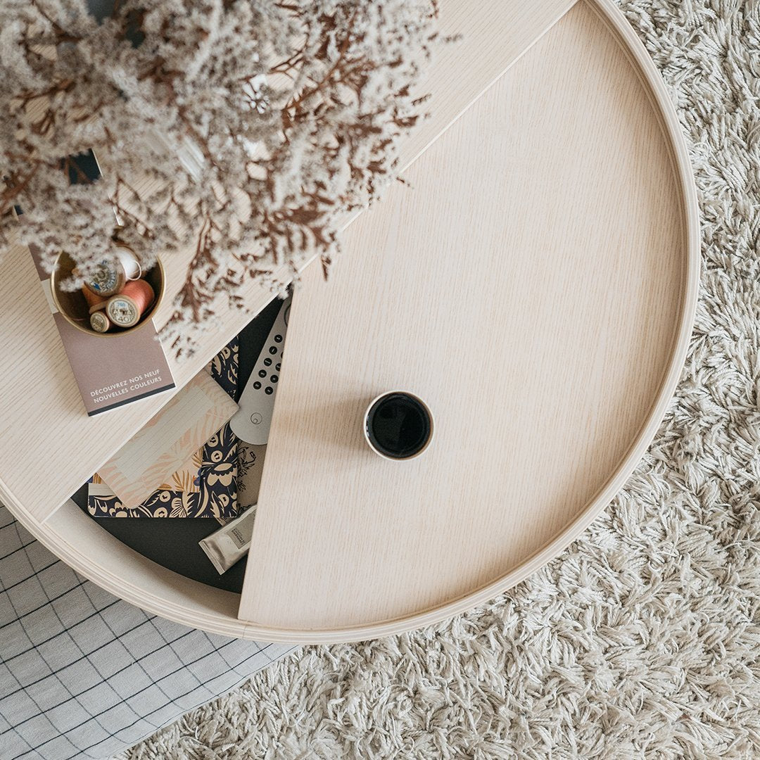 Light wood round coffee table with warm beige tones and geometric patterns on other items, surrounded by soft textured rug.