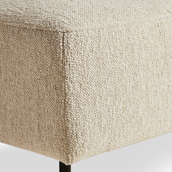 Textured beige fabric ottoman corner with a subtle, woven pattern and sleek black legs. Ideal for modern decor.