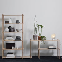 Natural wood shelving unit with sleek black and white accents, featuring green plants and soft neutral tones.
