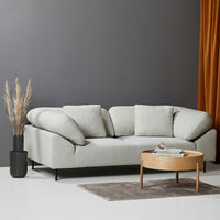 Light gray textured sofa with plush cushions, set against a dark wall and accented by warm amber curtains.