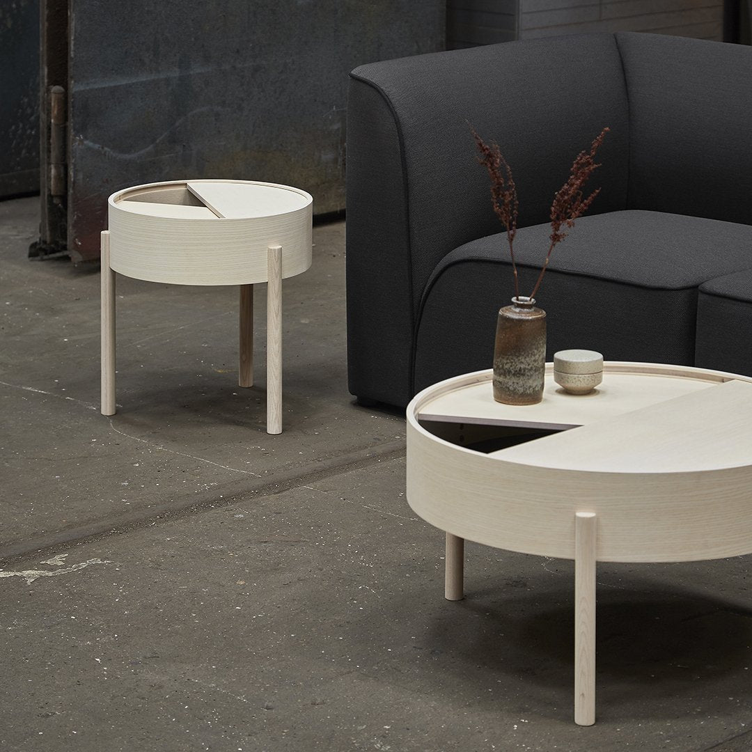 Modern round side tables in white with minimalistic design and contrasting black accents, set against a dark sofa.