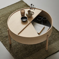 Light natural wood circular coffee table with a divided top, paired with a textured green and black patterned rug.