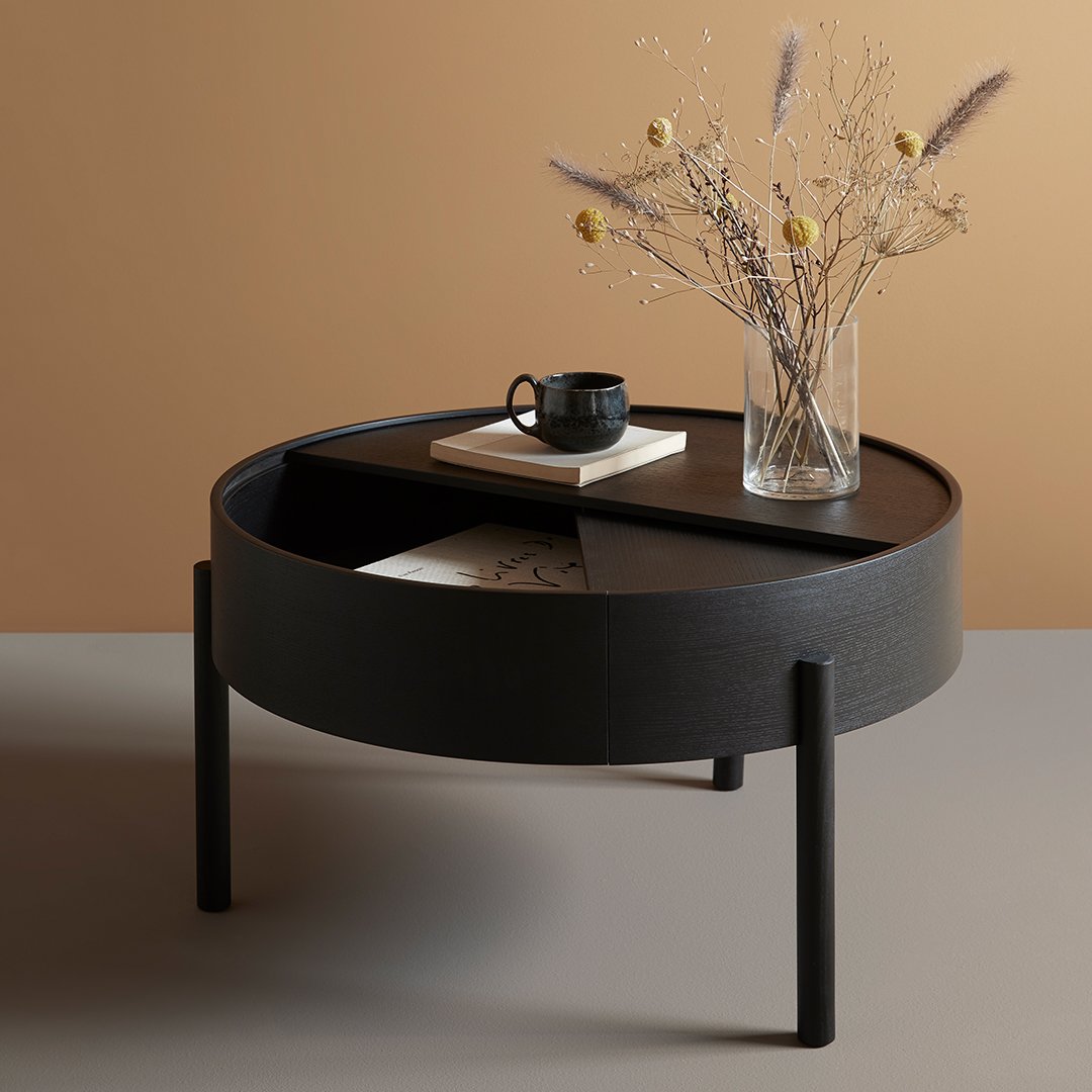 Black round coffee table with smooth, matte finish and geometric pattern, set against a warm, beige background.