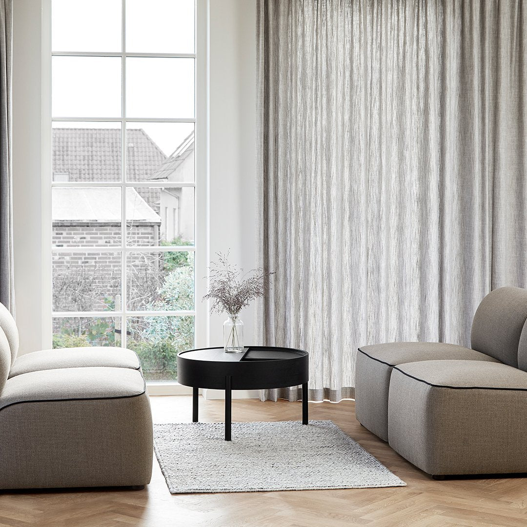 Modern gray and beige upholstered furniture with striped curtains against a light wood floor and a black round table.