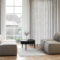 Modern gray and beige upholstered furniture with striped curtains against a light wood floor and a black round table.