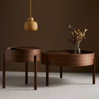 "Two round, dark brown wooden tables with smooth finishes, paired with a soft yellow pendant light."