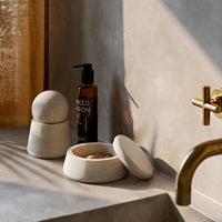 Grey stone containers with a smooth finish, accented by warm sunlight and a minimalist gold faucet.