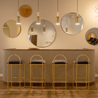 Modern gold bar stools with gray cushions paired with circular mirrors and warm wall tones in a chic setting.