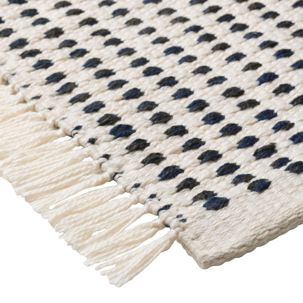 "Beige woven rug featuring navy blue and black dotted patterns with fringe edges."