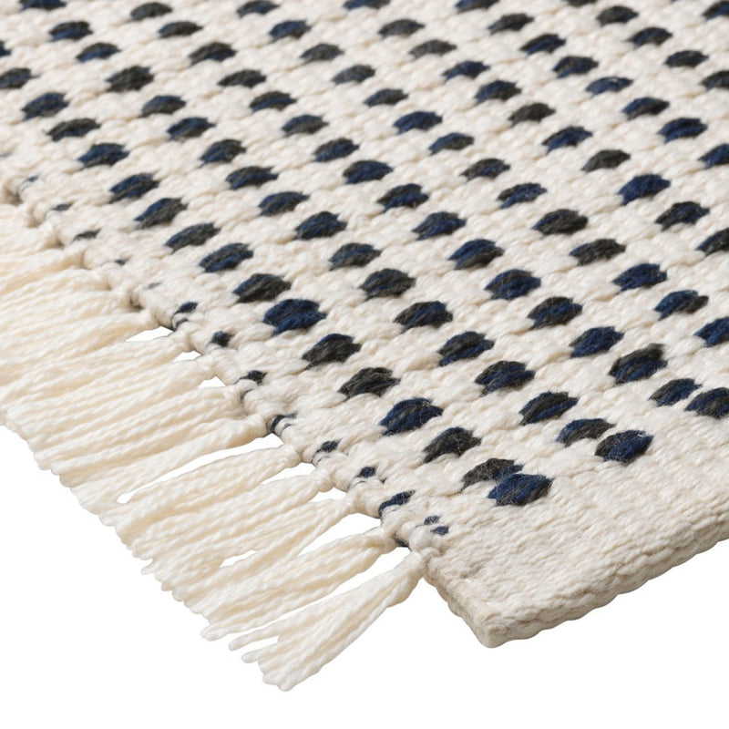 "Beige woven rug featuring navy blue and black dotted patterns with fringe edges."