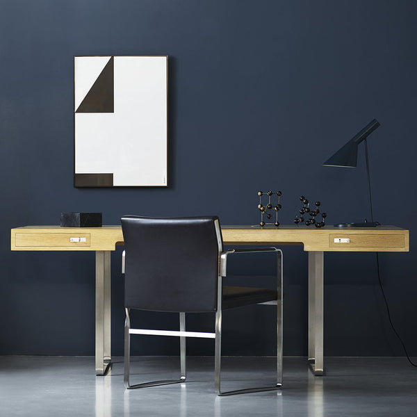 Modern desk in natural wood with sleek silver accents, set against a deep blue wall and minimalistic black and white art.