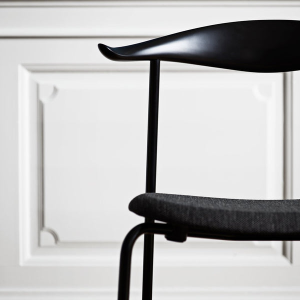 Black chair with a curved backrest and gray upholstery against a white paneled background.