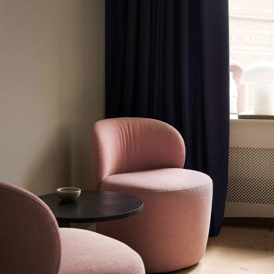Soft pink curved chairs with black curtains and a minimalist black table, creating a modern, cozy atmosphere.
