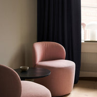 Soft pink curved chairs with black curtains and a minimalist black table, creating a modern, cozy atmosphere.