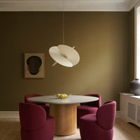 Modern dining area featuring burgundy chairs, a round marble table, and a sleek white pendant light against an olive green wall.