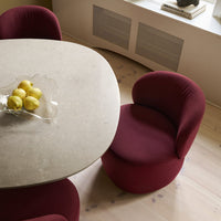 Curved burgundy chair beside a light stone table, set on pale wood flooring with subtle pattern detailing.