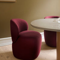 Modern burgundy chair with soft curves, paired with a light stone table and earthy green walls, creating a cozy ambiance.