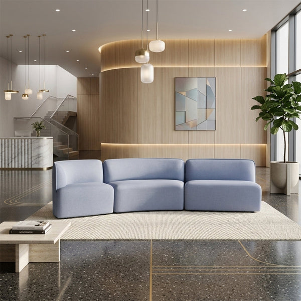 Light blue sectional sofa on a soft beige area rug, with a sleek modern backdrop and warm wood accents.