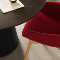 Red upholstered chair with a smooth, curved design next to a dark wooden table on a light-colored floor.