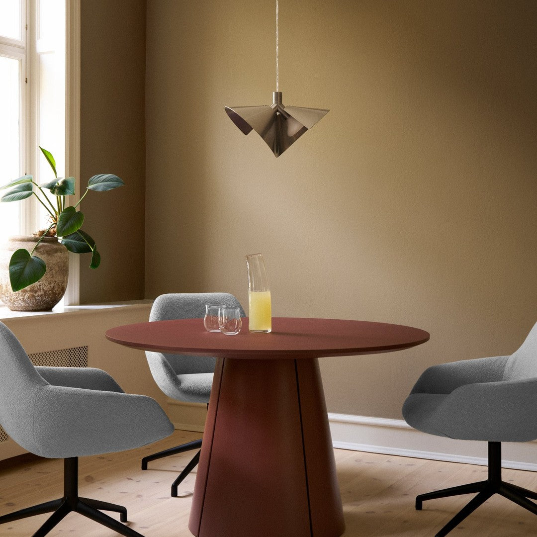 Gray upholstered chairs around a round, rust-colored table with a modern pendant light in a warm-toned room.